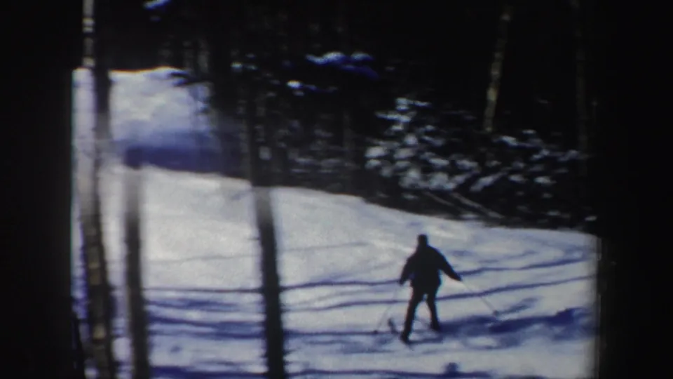 A skier descends through a wooded New Hampshire snow slope, seen from a home-movie camera behind trees in 1962.