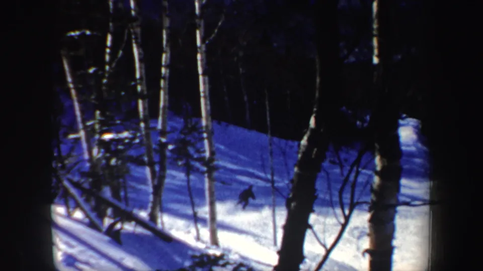 1962 New Hampshire 8mm frame with a lone skier crossing a sunlit patch of snow in a wooded hillside scene.