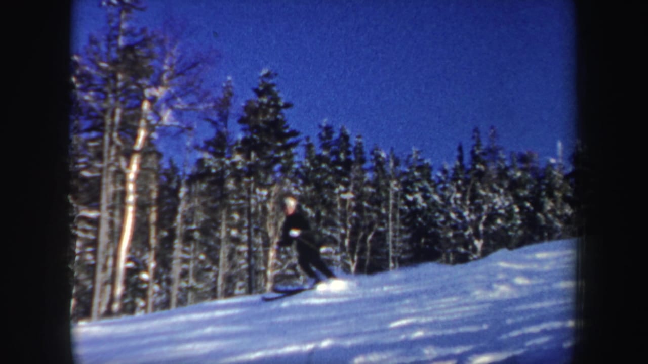 A skier in dark winter gear moves across a snowy New Hampshire forest slope in 1962 home-movie footage.