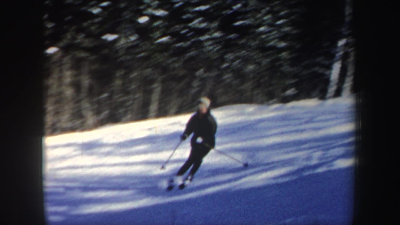 The skier descends a bright snowy trail bordered by evergreens in 1962 New Hampshire 8mm footage.