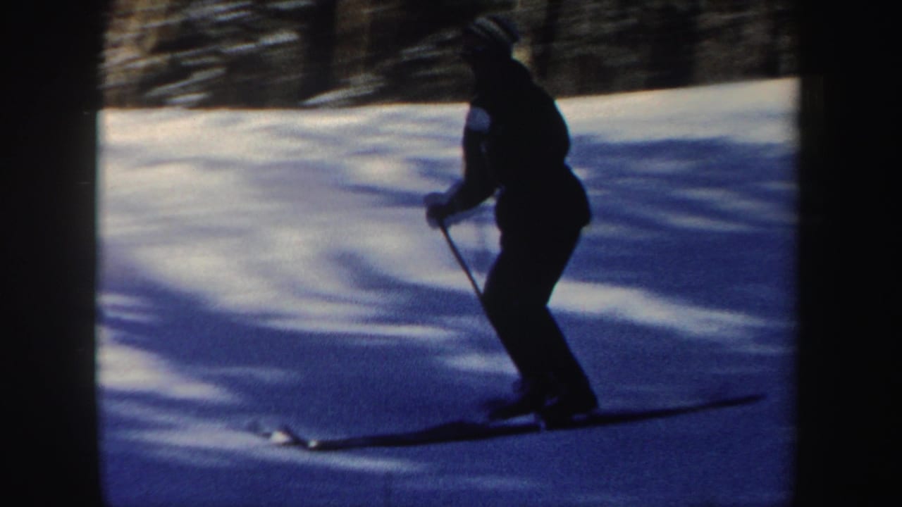 A closer side view shows the skier using poles while moving over packed snow on a forested New Hampshire slope.