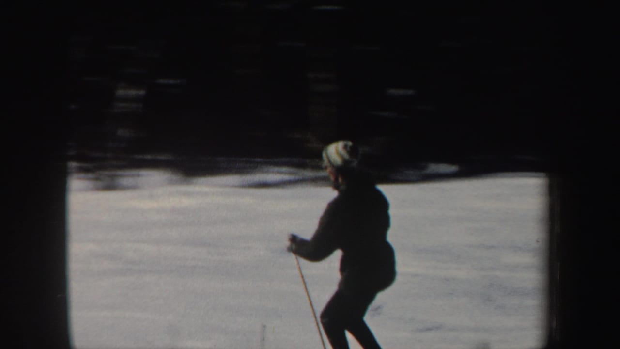 Skier in a dark coat and light hat moves across a snowy slope.