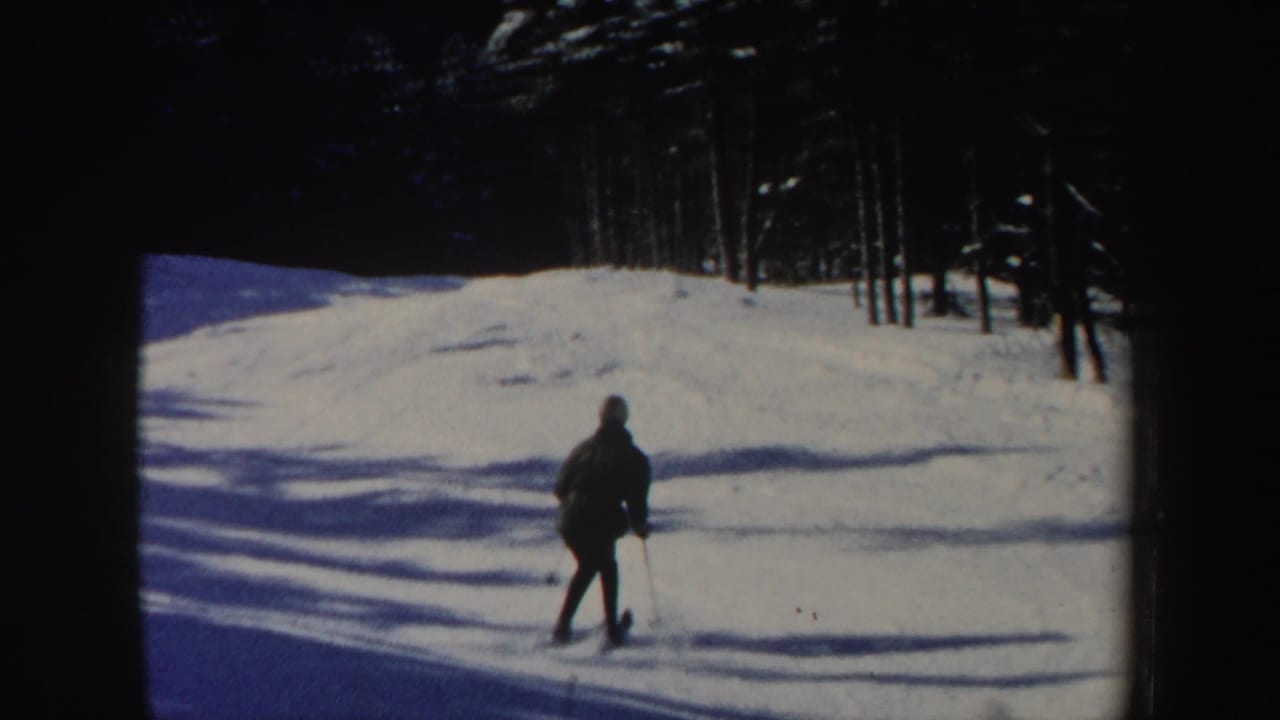 A distant skier descends a sunlit New Hampshire snow slope, with long shadows and trees along the upper edge.