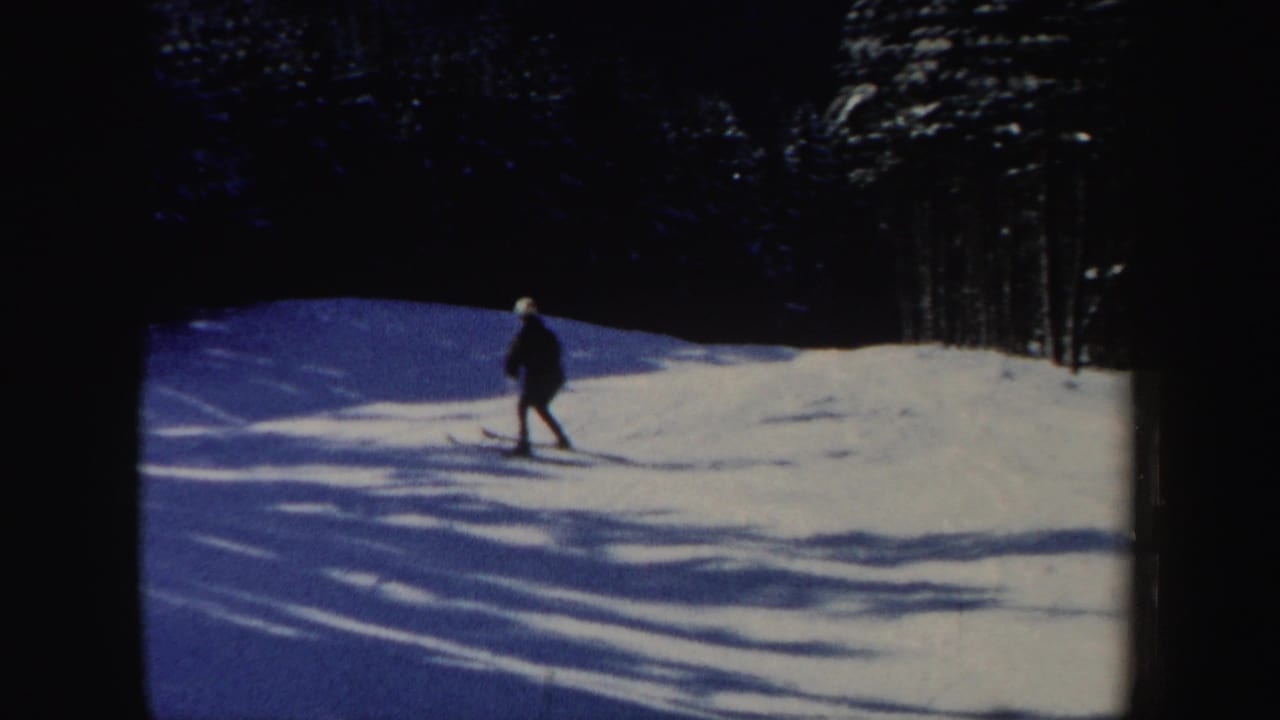The skier appears small in the frame while crossing a snowy hillside with pronounced tree shadows in 1962 New Hampshire footage.