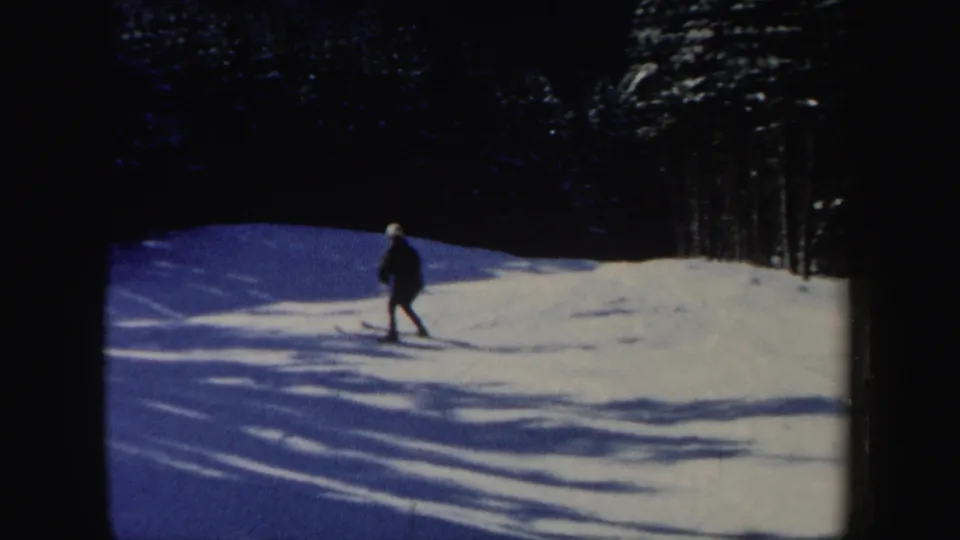 The skier appears small in the frame while crossing a snowy hillside with pronounced tree shadows in 1962 New Hampshire footage.