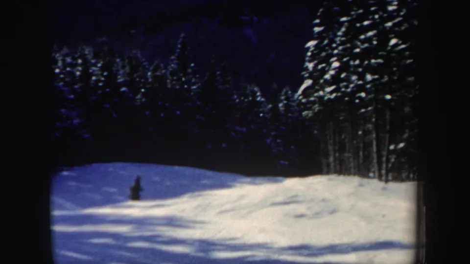 1962 New Hampshire 8mm frame showing a snowy wooded ski slope with a small distant skier under a blue winter sky.