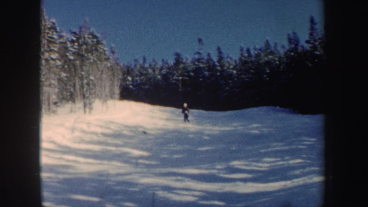 1962 New Hampshire 8mm frame with a skier descending a snowy slope between snow-covered evergreens and a dark wooded edge.