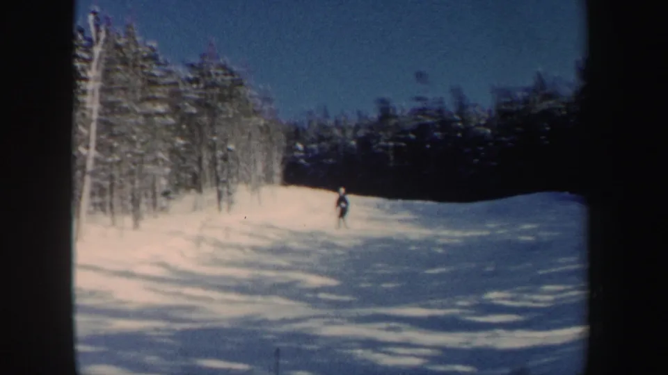 A distant skier moves down a wooded snowy slope in 1962 New Hampshire home-movie footage.