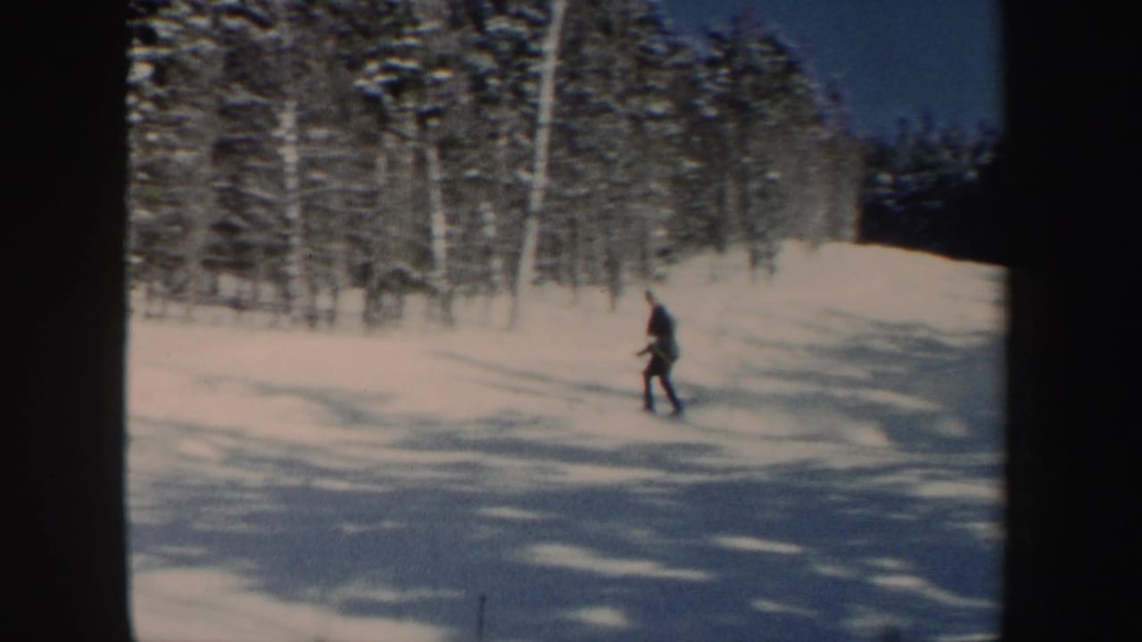 The skier continues downhill near snow-covered trees, filmed with soft 8mm color and handheld framing.