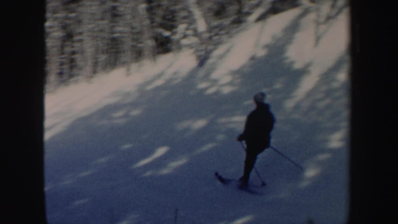 A skier appears in silhouette on a blue-shadowed snowy hillside in 1962 New Hampshire footage.