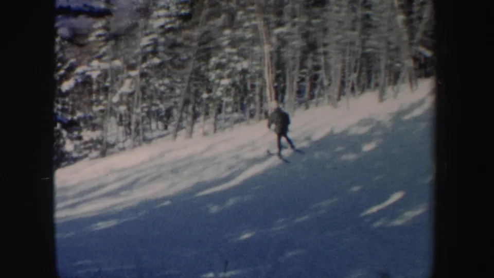 A skier moves downhill through a snowy New Hampshire forest setting in early-1960s 8mm footage.