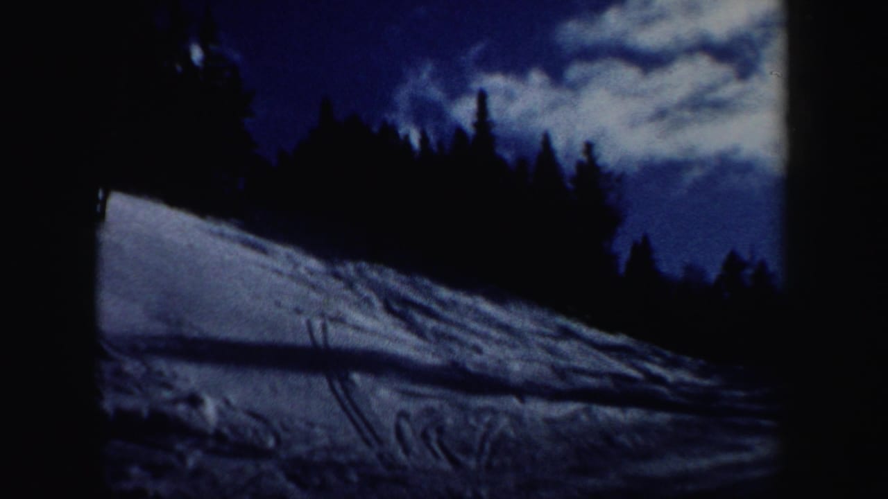 1962 New Hampshire 8mm frame showing a snowy ski slope bordered by dark evergreens under a blue, clouded sky.