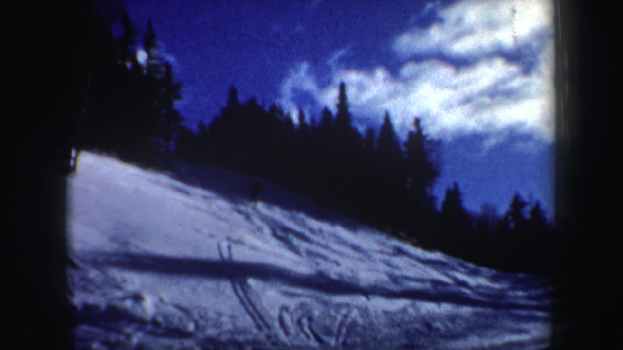 1962 New Hampshire winter scene with a tracked snow slope, evergreen trees, and bright cloud cover above.