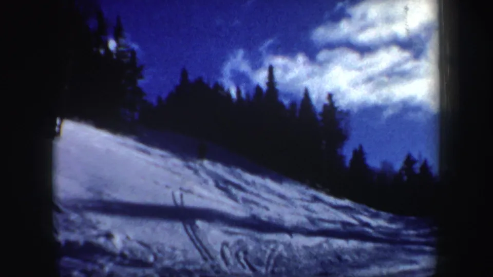 1962 New Hampshire winter scene with a tracked snow slope, evergreen trees, and bright cloud cover above.