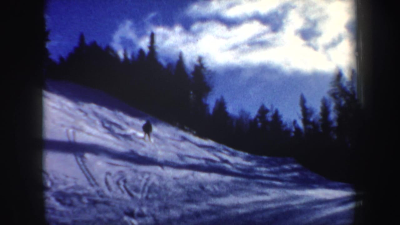 1962 New Hampshire 8mm frame with a lone distant skier moving downhill across a snowy, forest-lined slope.
