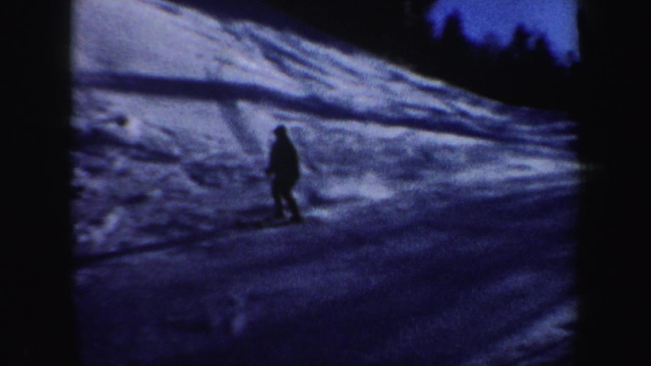 A skier in silhouette continues downhill on a snowy New Hampshire slope, with trees and ski tracks visible in the background.