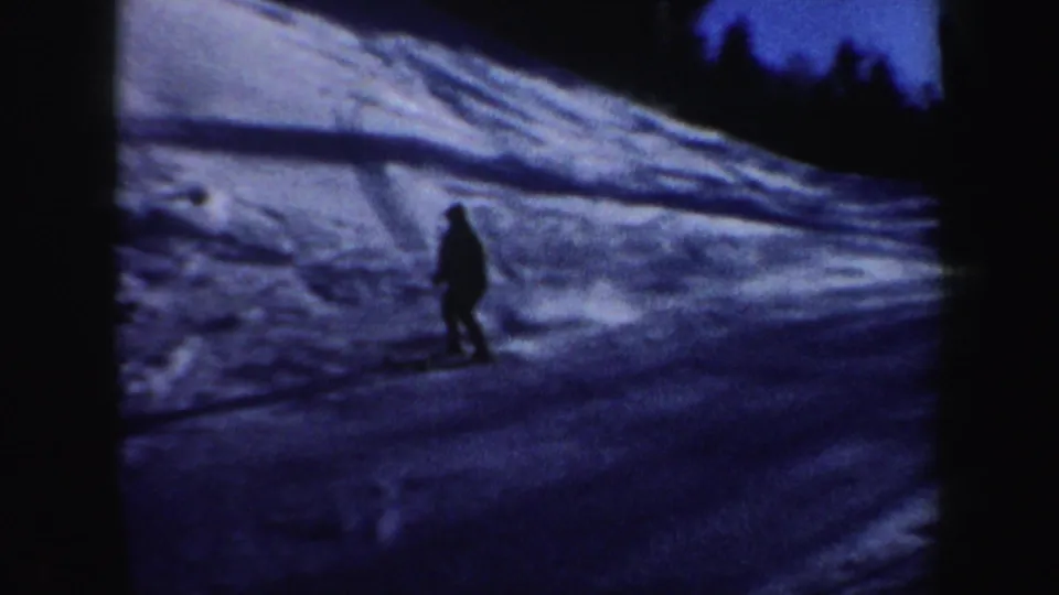 A skier in silhouette continues downhill on a snowy New Hampshire slope, with trees and ski tracks visible in the background.