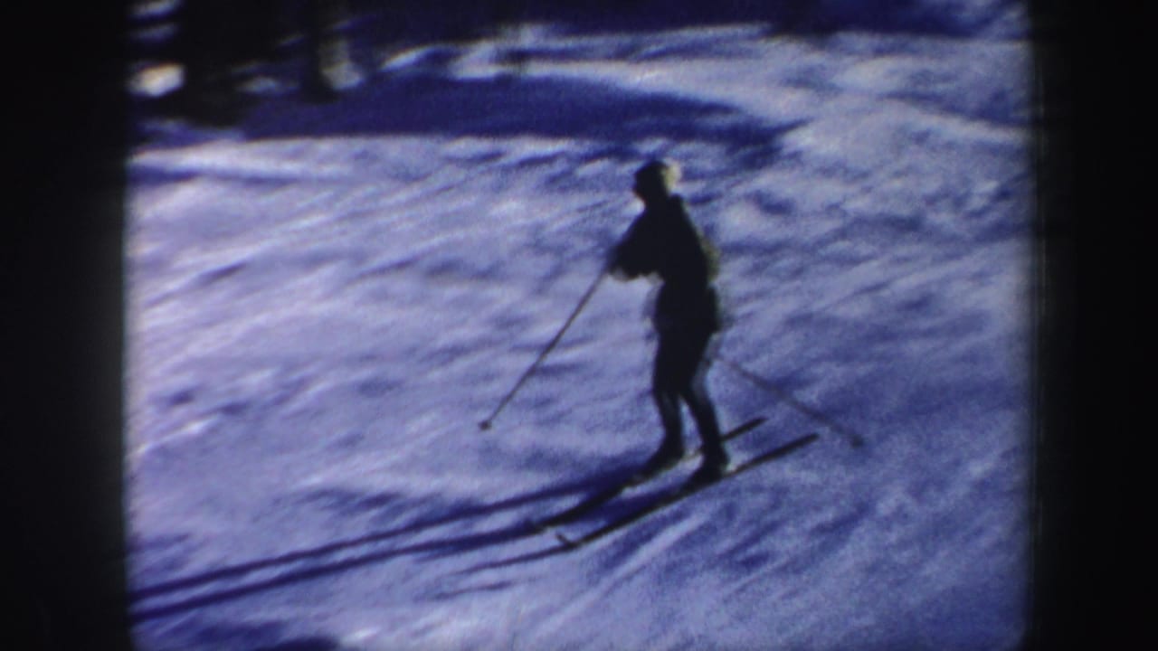 A closer home-movie view shows the skier using poles while descending a blue-tinted snowy slope in New Hampshire.