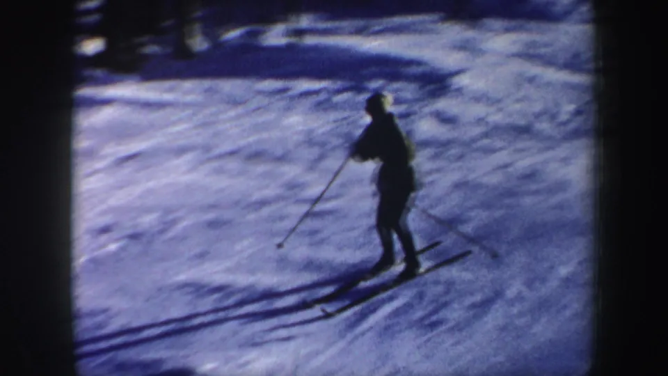 A closer home-movie view shows the skier using poles while descending a blue-tinted snowy slope in New Hampshire.
