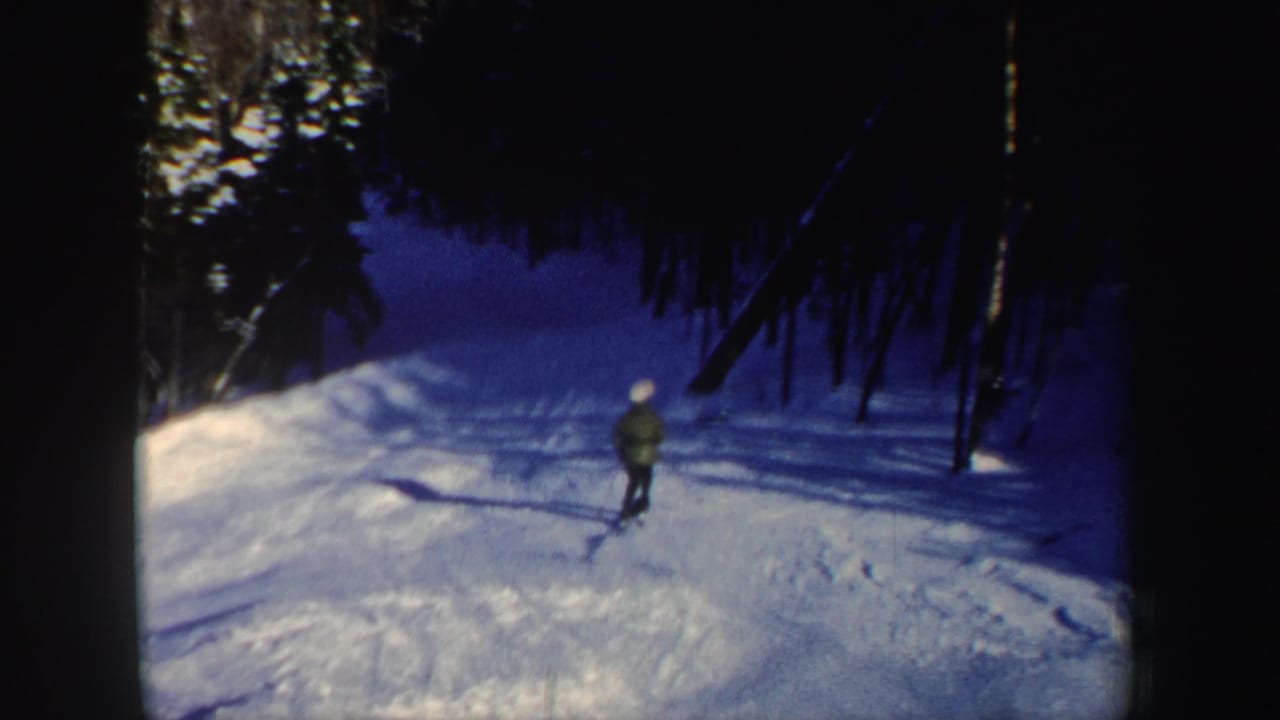 The lone skier continues downhill on a wooded New Hampshire snow slope, with tree shadows stretching across the trail.