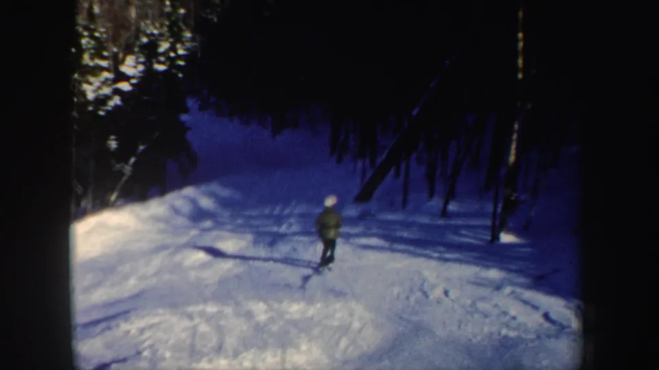 The lone skier continues downhill on a wooded New Hampshire snow slope, with tree shadows stretching across the trail.