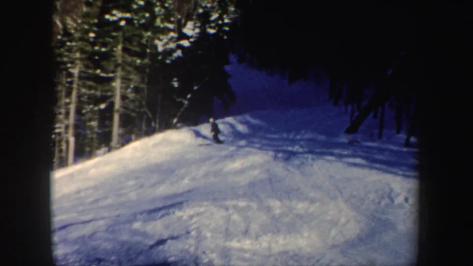 Near the end of the clip, the skier is distant on the New Hampshire slope, leaning slightly as the wooded trail curves through shadow.