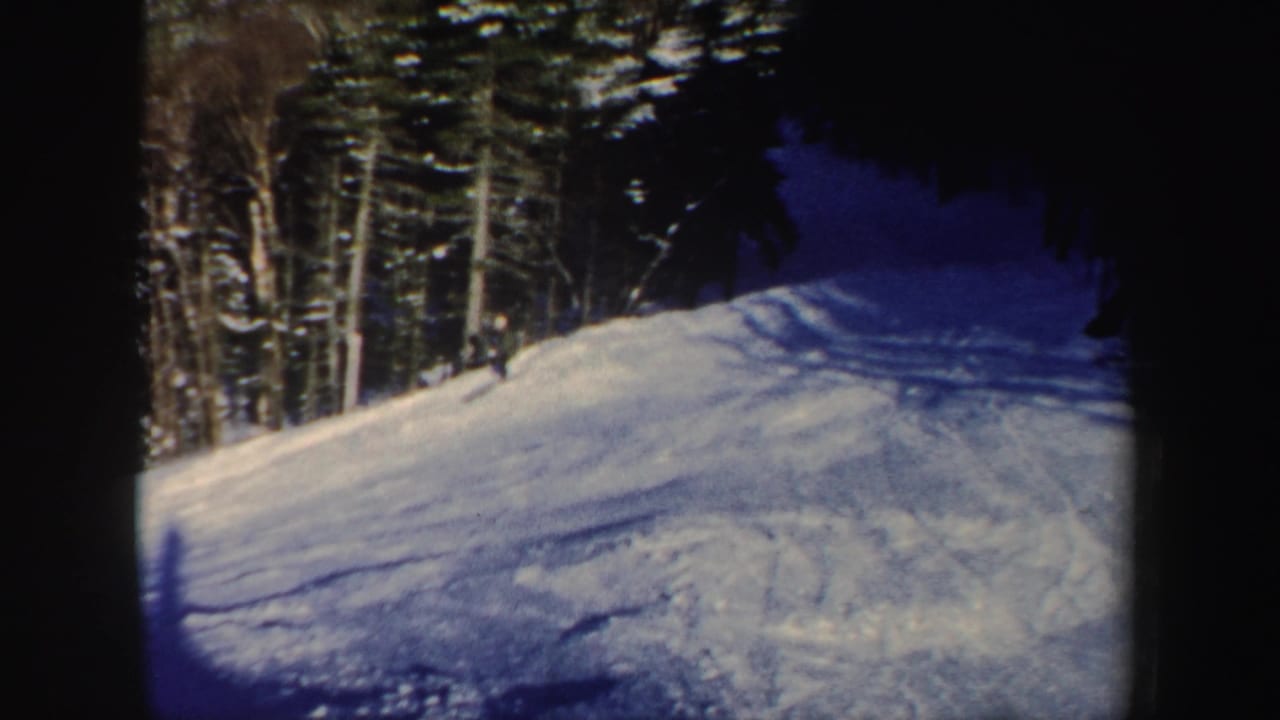 1962 New Hampshire 8mm frame showing a distant skier on a bright snowy slope beside dark evergreen and bare trees.