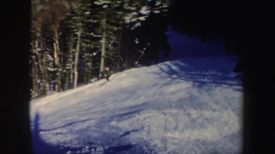1962 New Hampshire 8mm frame showing a distant skier on a bright snowy slope beside dark evergreen and bare trees.