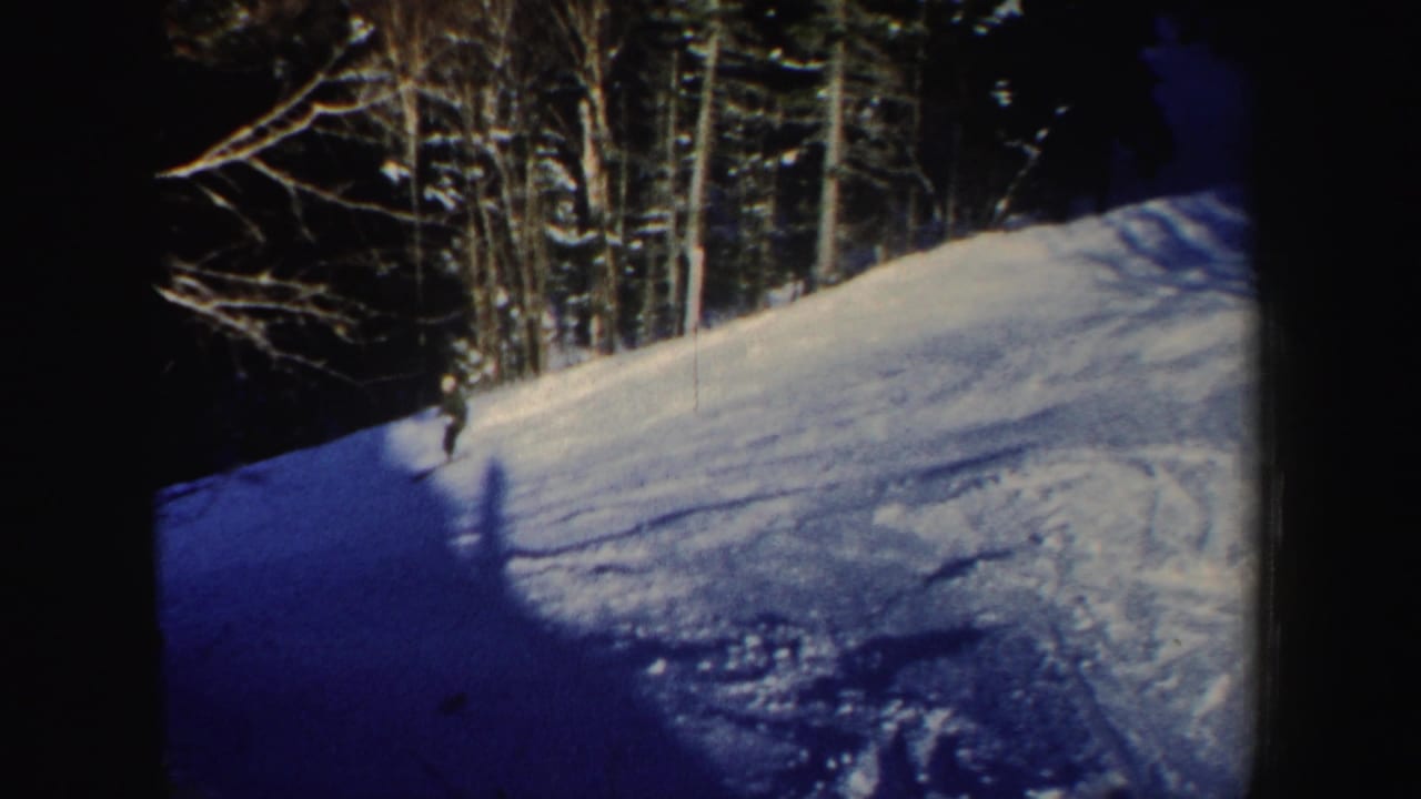 A distant skier crosses a New Hampshire snow slope toward shade, with dark evergreens and bare trees framing the run.