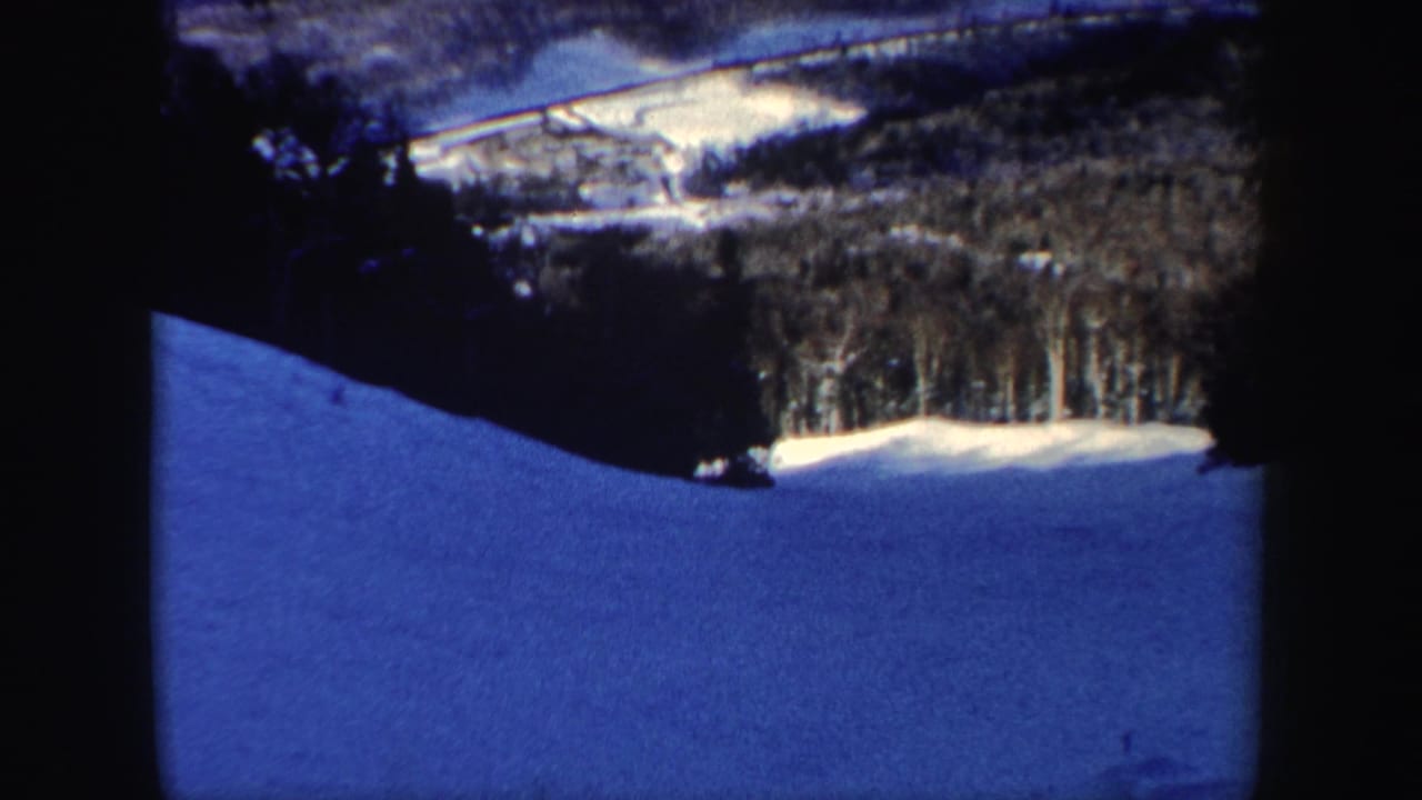 The skier is farther down the New Hampshire slope, seen against blue-shadowed snow and a band of winter forest.