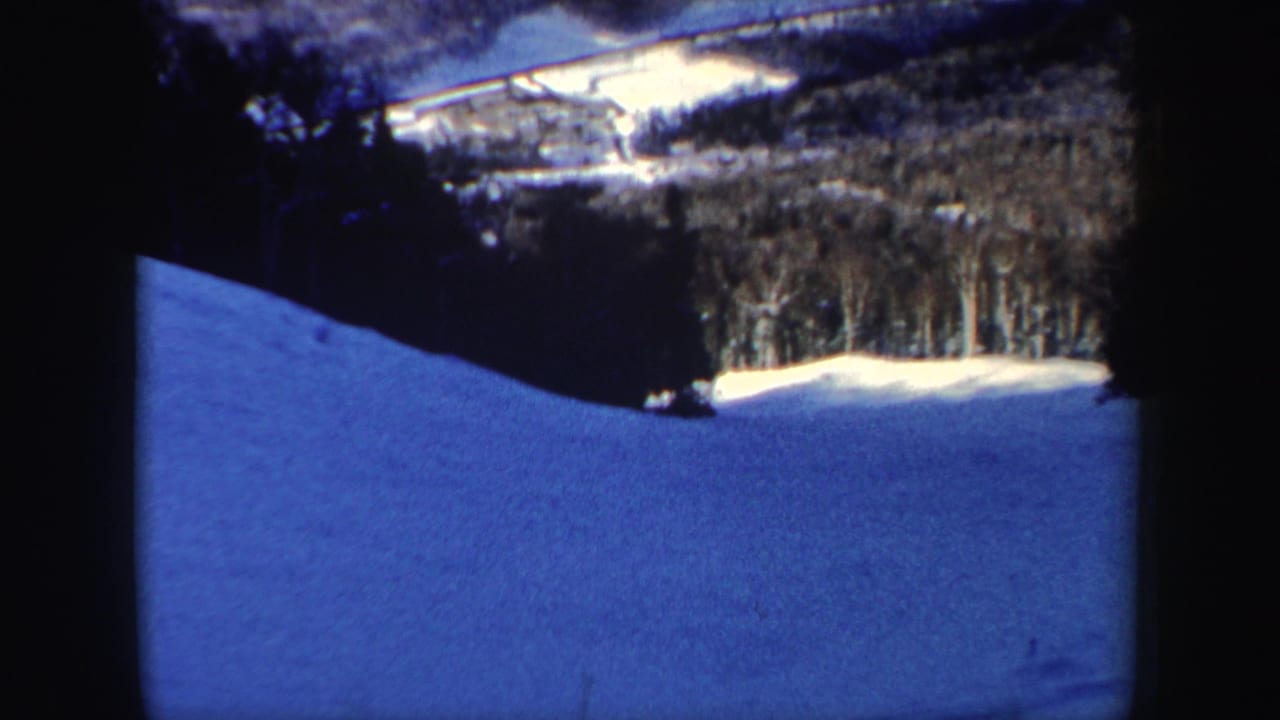 Final 8mm frame shows the skier small on a broad blue-toned snowfield below New Hampshire winter woods.