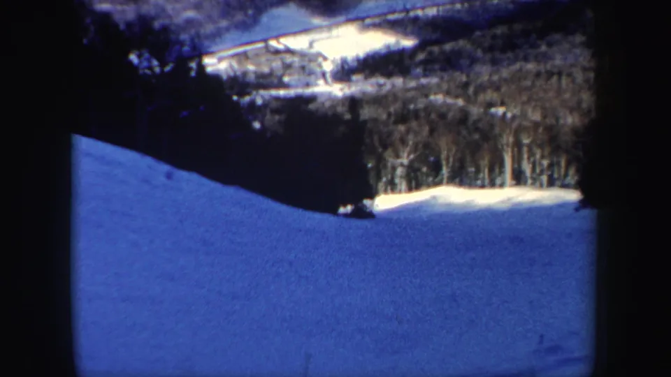 Final 8mm frame shows the skier small on a broad blue-toned snowfield below New Hampshire winter woods.