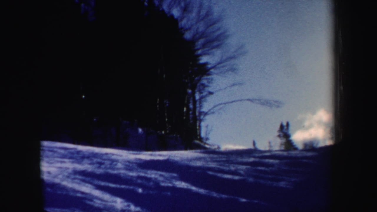 1962 New Hampshire 8mm frame showing a snowy wooded ski slope under bright winter sky.