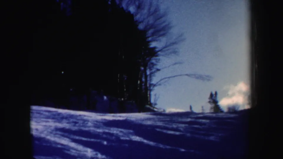 1962 New Hampshire 8mm frame showing a snowy wooded ski slope under bright winter sky.