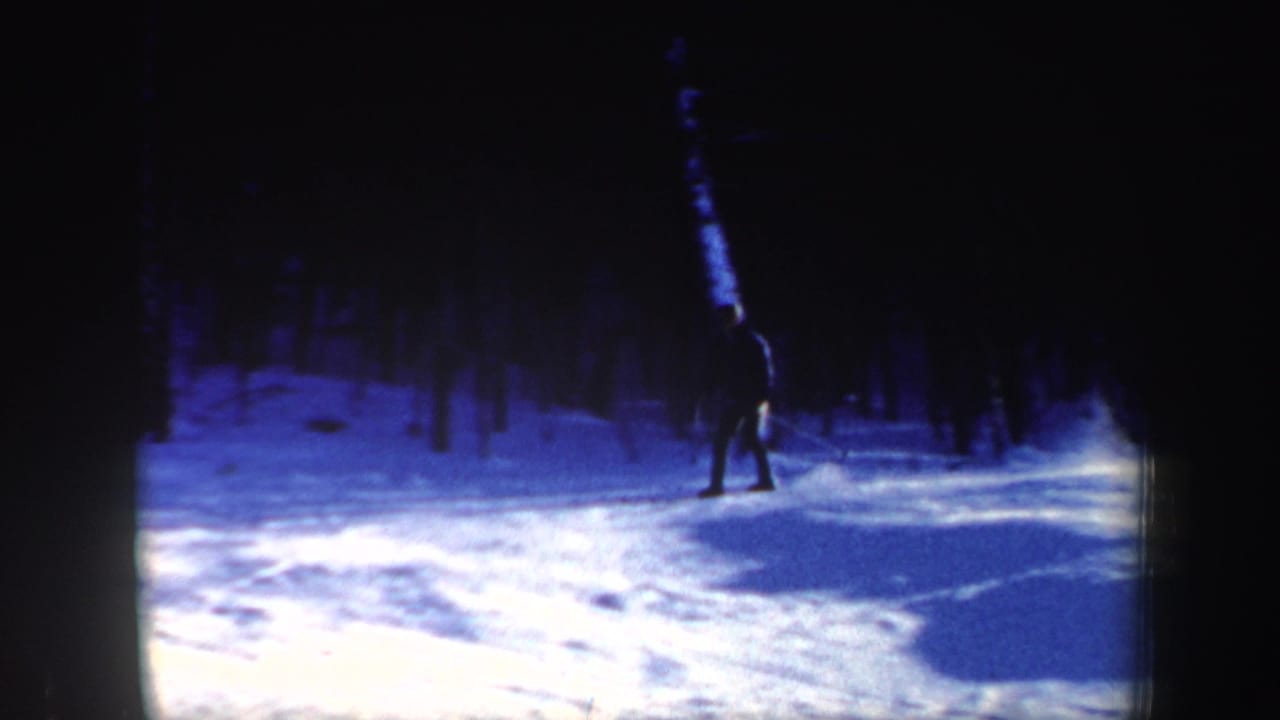 A lone skier in dark clothing crosses a snowy New Hampshire wooded slope in 1962 home-movie footage.