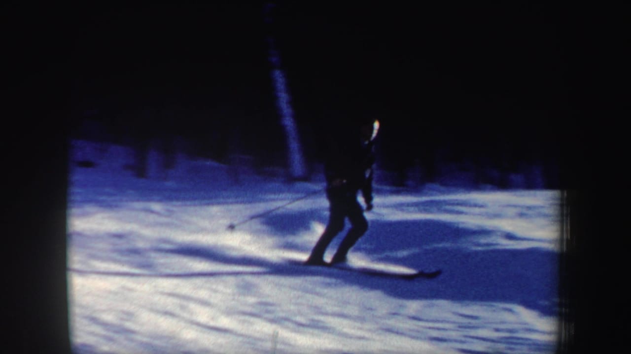 A lone skier descends a wooded New Hampshire snow slope, captured in blue-toned 8mm film.