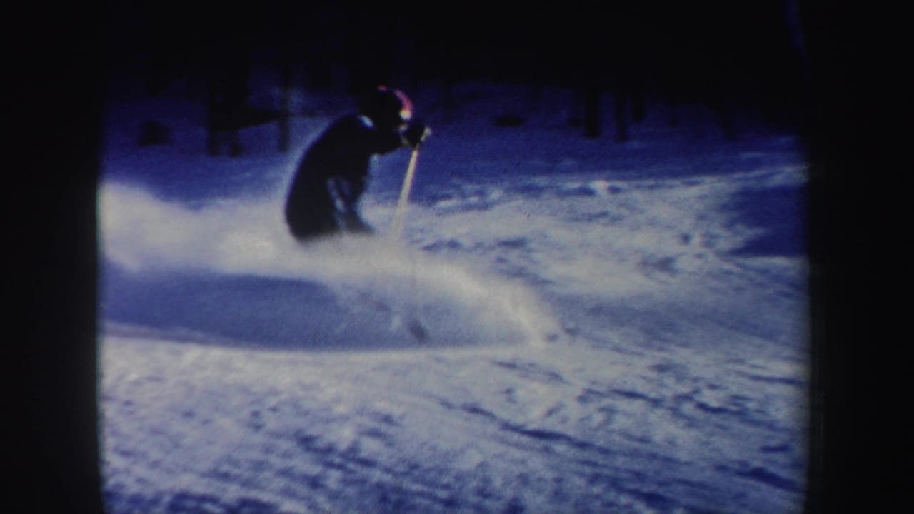 A skier in New Hampshire home-movie footage descends a snowy wooded slope, partly silhouetted against blue-toned snow.