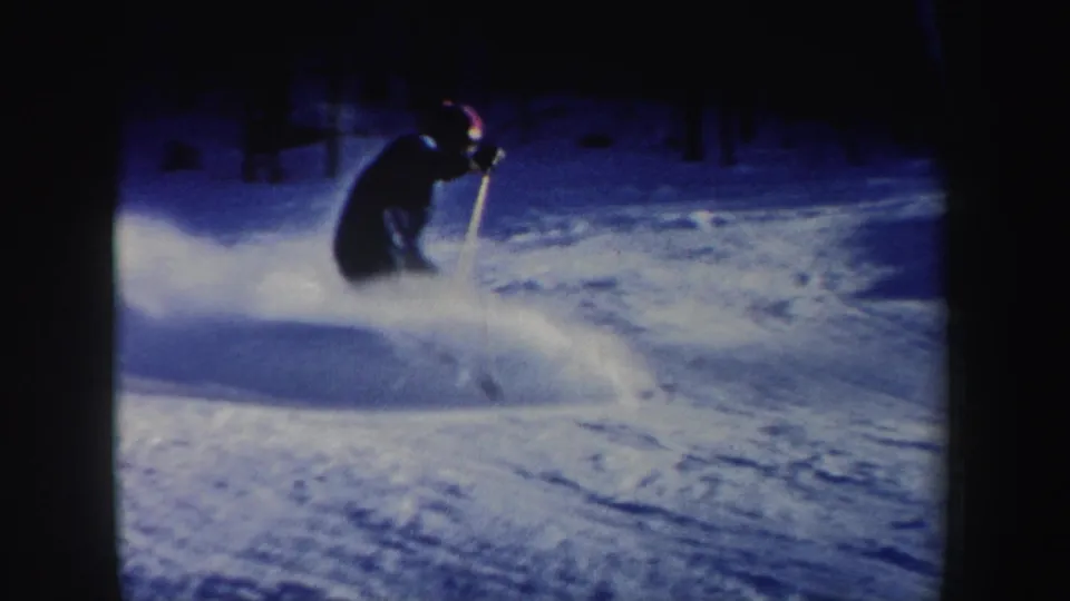 A skier in New Hampshire home-movie footage descends a snowy wooded slope, partly silhouetted against blue-toned snow.