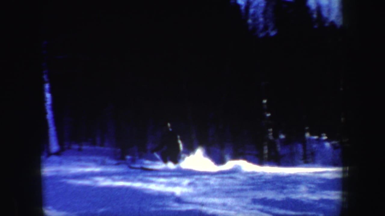 A skier stops sharply on a wooded New Hampshire slope, kicking up a bright plume of snow in blue-toned 8mm footage.