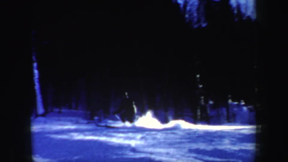 A skier stops sharply on a wooded New Hampshire slope, kicking up a bright plume of snow in blue-toned 8mm footage.