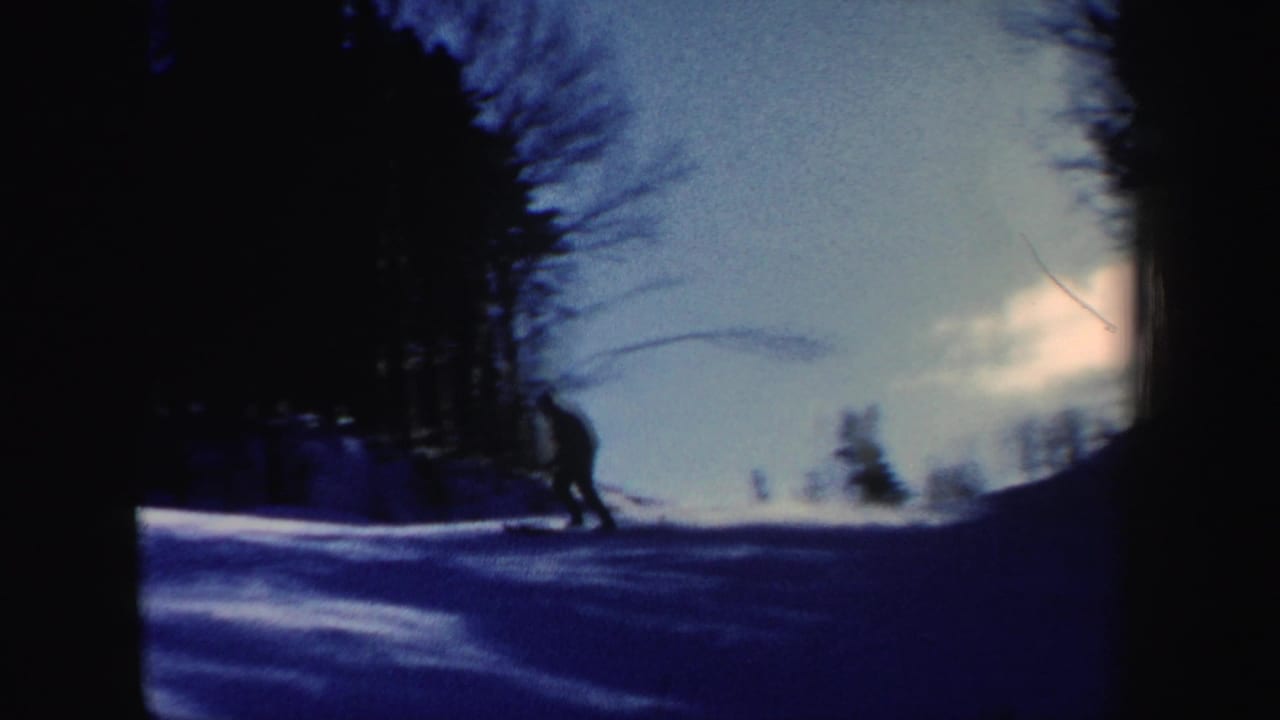 A distant skier crosses a dim, blue-tinted snowy hillside with trees in 1962 New Hampshire 8mm footage.