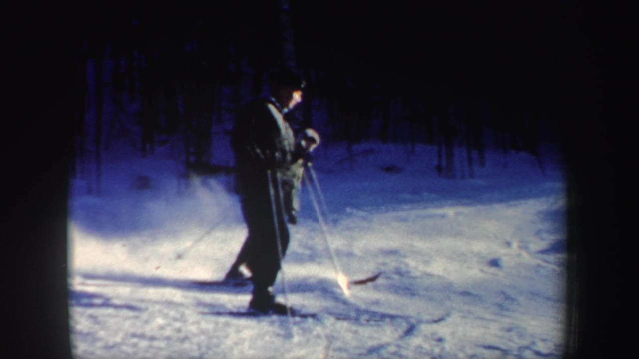 A skier slows or stands with poles on a snowy New Hampshire slope, with woods and soft 8mm grain behind them.