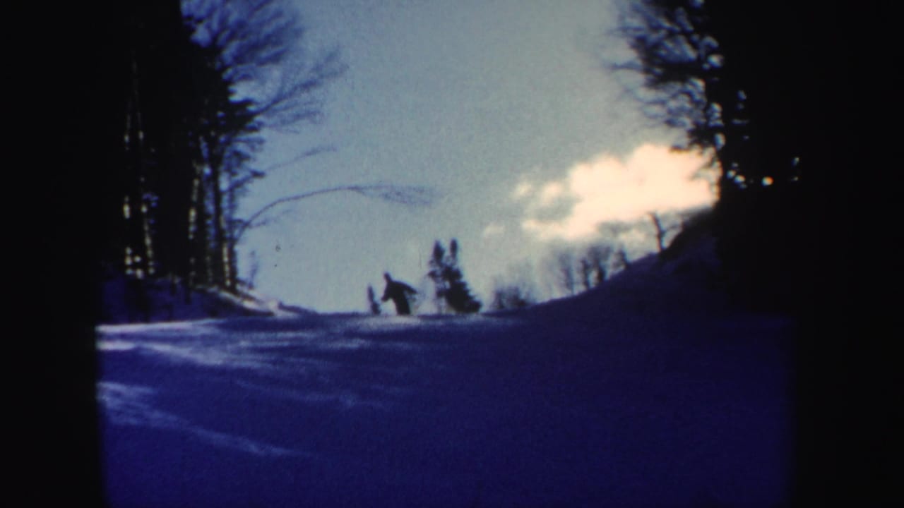 1962 New Hampshire 8mm frame showing a distant skier on a snow-covered slope bordered by bare trees and dark forest.
