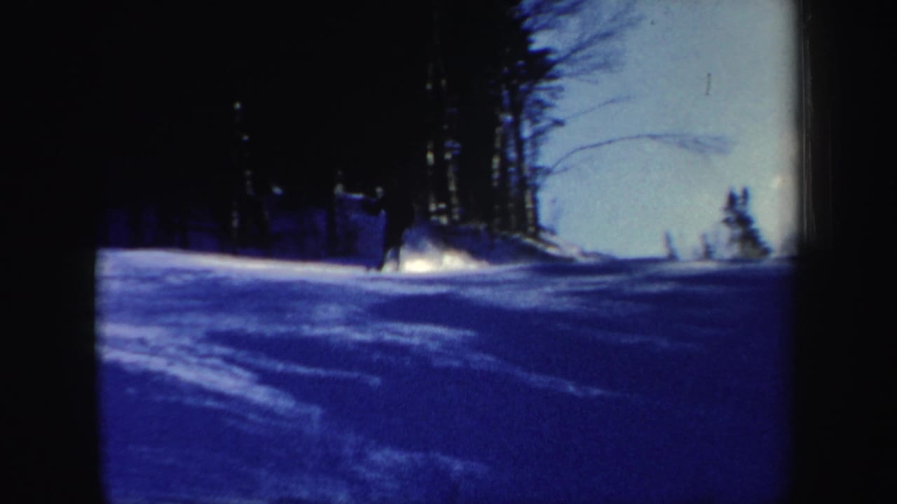 Blue-tinted 8mm view of a New Hampshire ski slope with snow glare, bare trees, and a distant figure near the upper right.