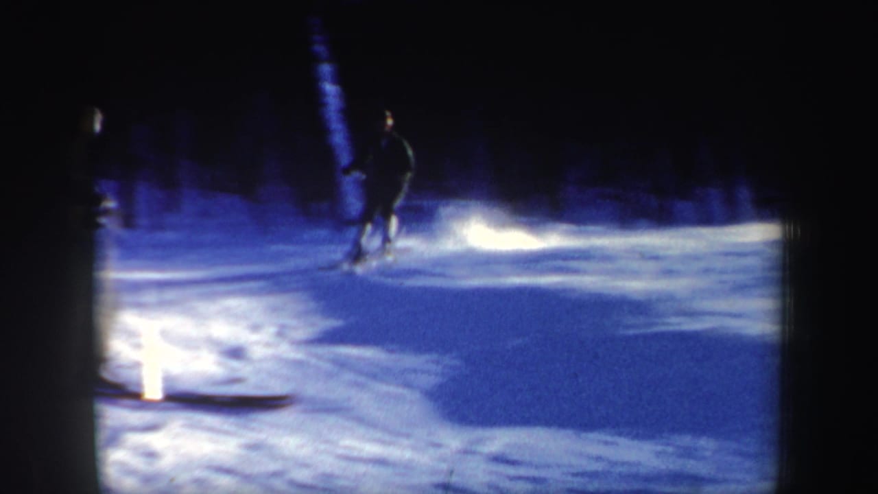 1962 home-movie frame of a skier crossing a blue-shadowed New Hampshire slope, with strong reflected light on the snow.
