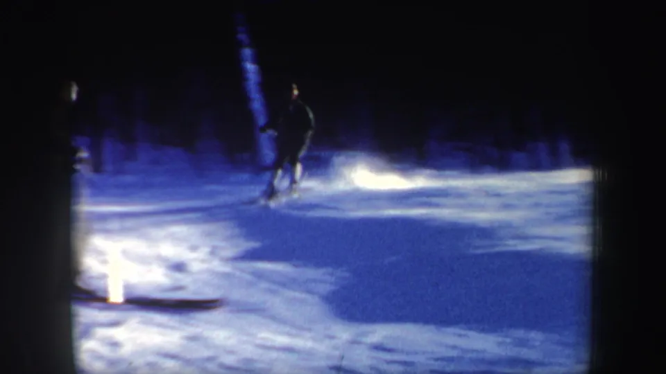 1962 home-movie frame of a skier crossing a blue-shadowed New Hampshire slope, with strong reflected light on the snow.