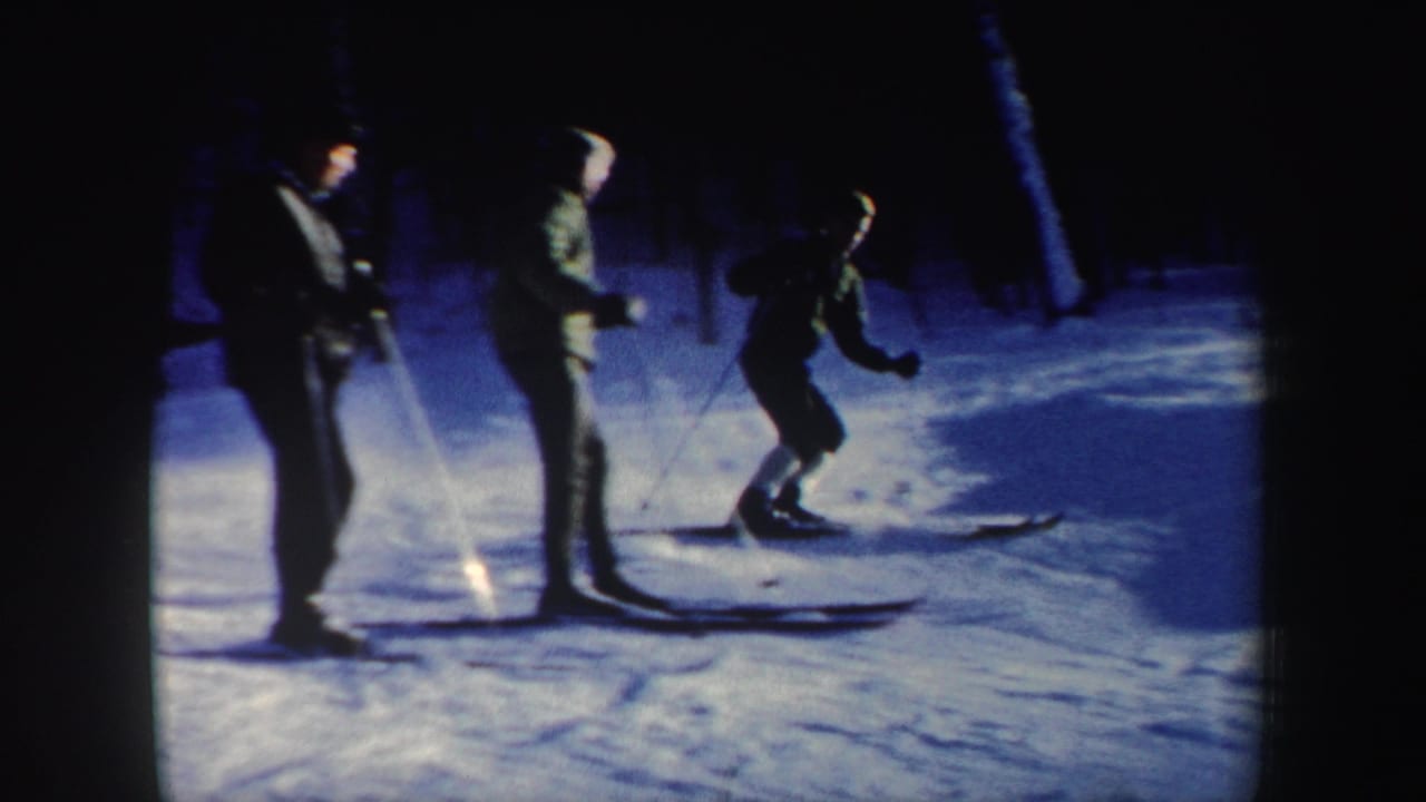 1962 New Hampshire 8mm frame showing three skiers on a snowy slope, with two standing near poles and another moving past.