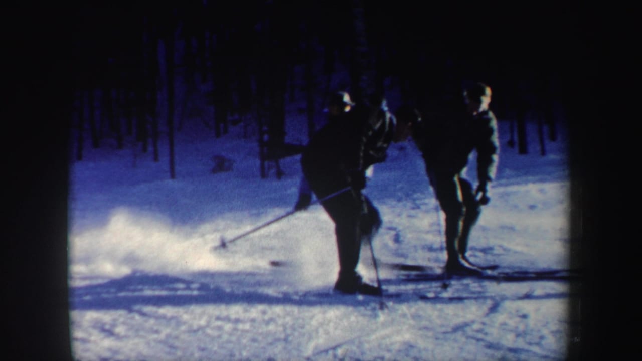 1962 New Hampshire frame of three skiers paused together on a snowy slope, silhouetted against blue-cast snow and trees.