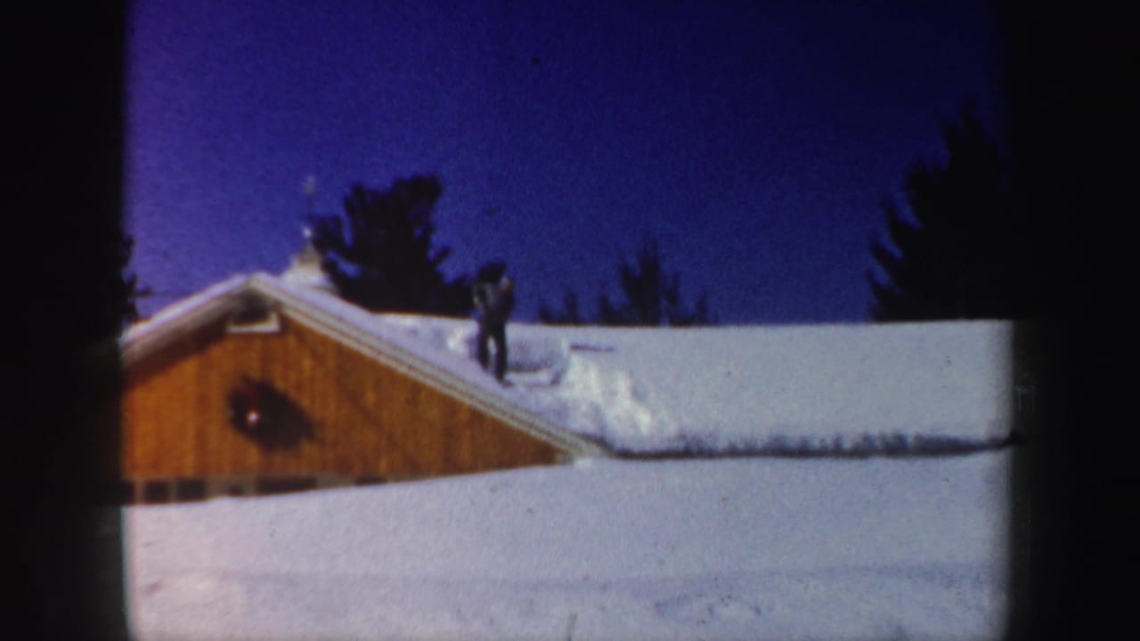 New Hampshire winter frame from 1962 showing a skier near a snow-covered wooden building under a deep blue sky.