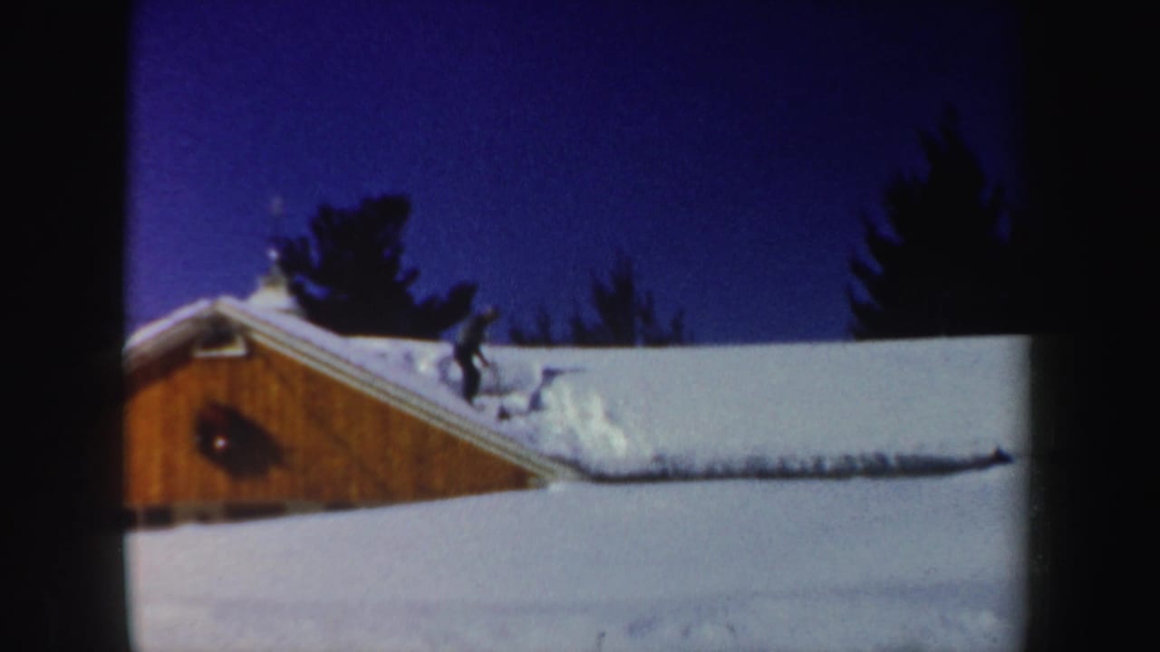 A man appears to use a tool to move snow on a sloped roof in snowy 1962 New Hampshire home-movie footage.
